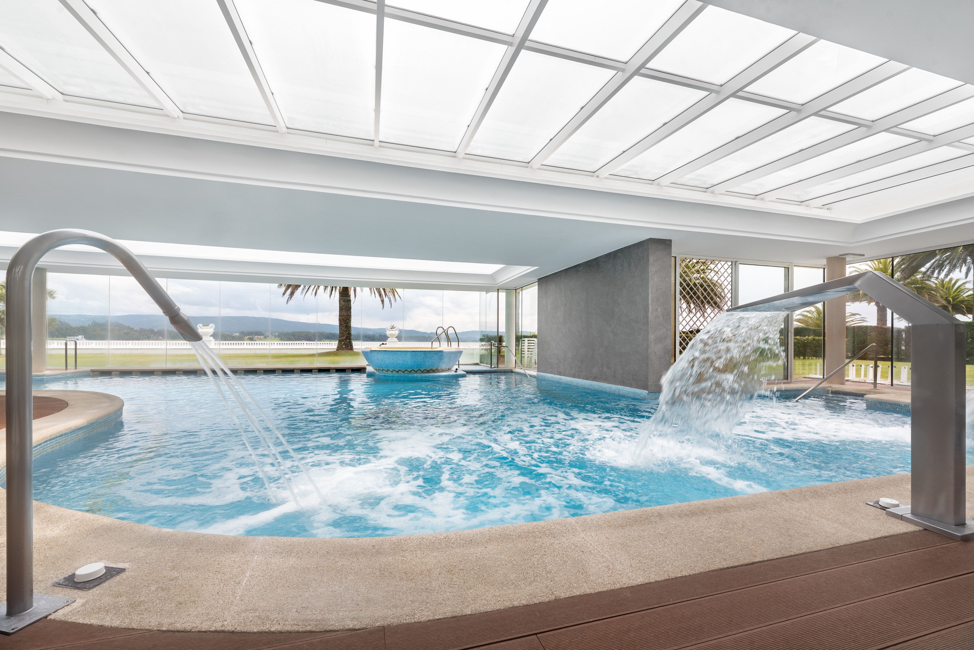 Een binnenzwembad met glazen dak, een jacuzzi en een waterval.