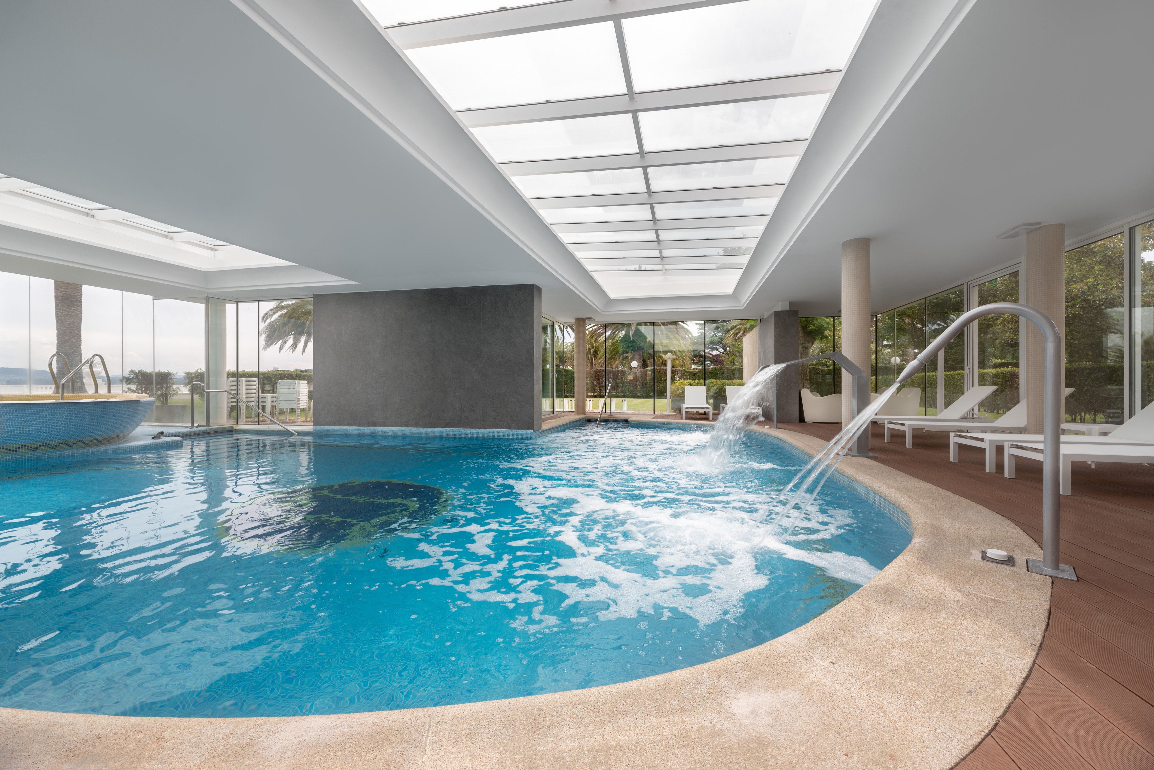 Una piscina interior con techo de cristal, agua cristalina y una pequeña cascada.