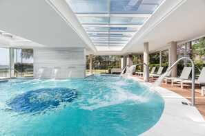 Une piscine intérieure moderne dotée d’un toit en verre, d’une eau cristalline et offrant une vue sur l’extérieur.