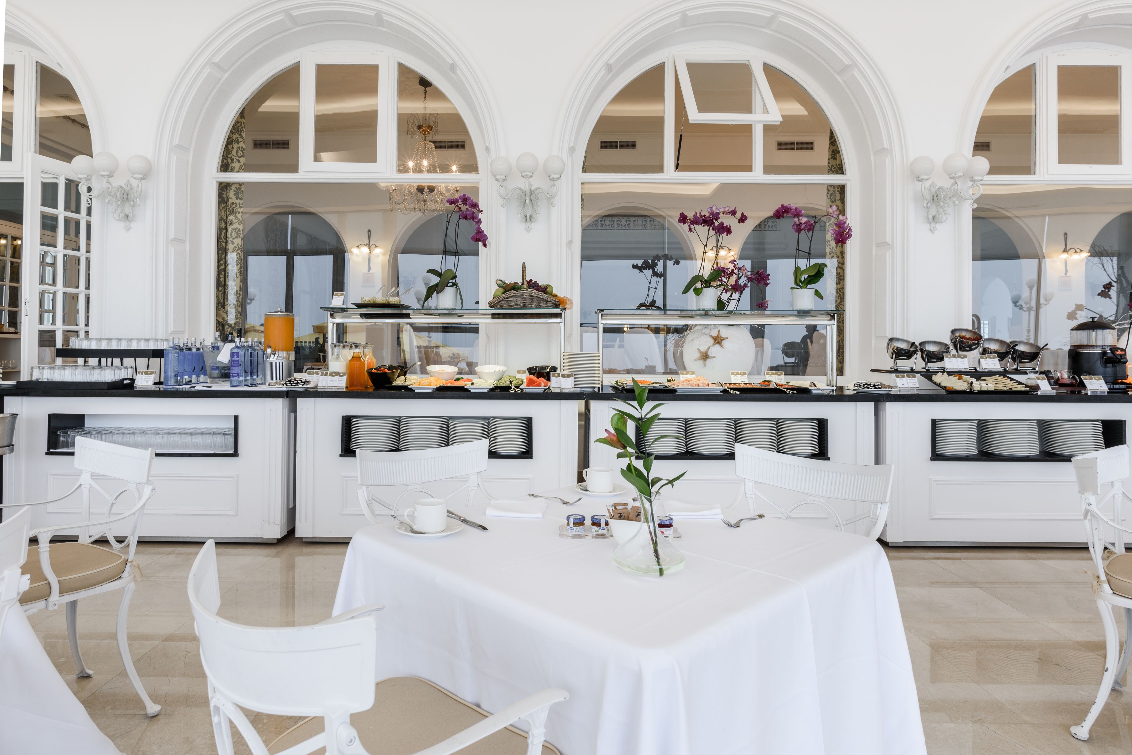 Un comedor amplio con mobiliario blanco, una barra libre y ventanas arqueadas grandes.