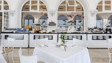 Un comedor amplio con mobiliario blanco, una barra libre y ventanas arqueadas grandes.