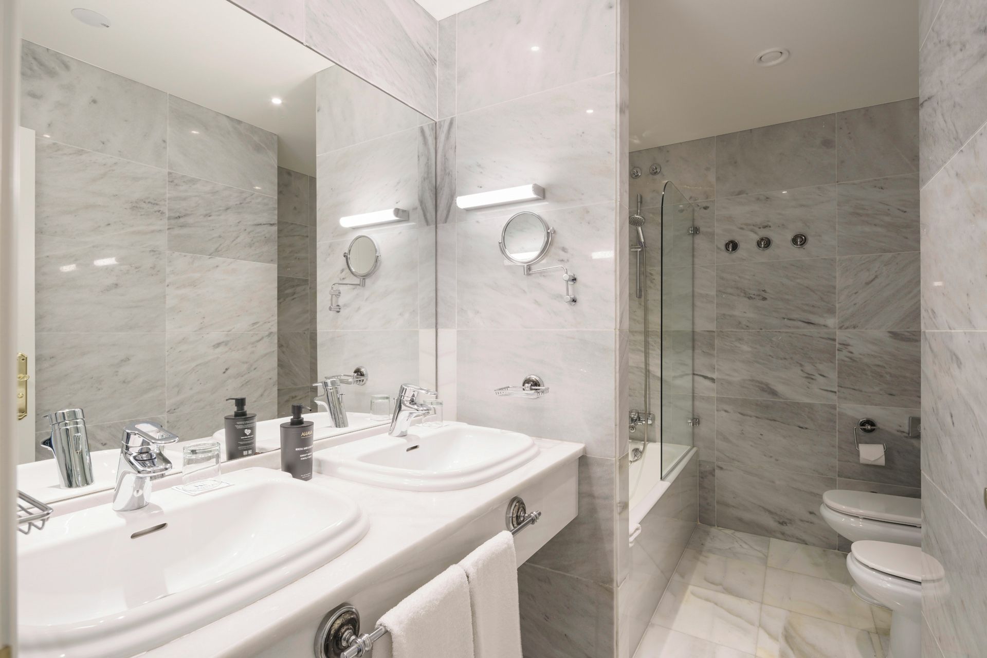 Un baño moderno con dos lavamanos, un espejo grande y una ducha con cerramiento de vidrio.