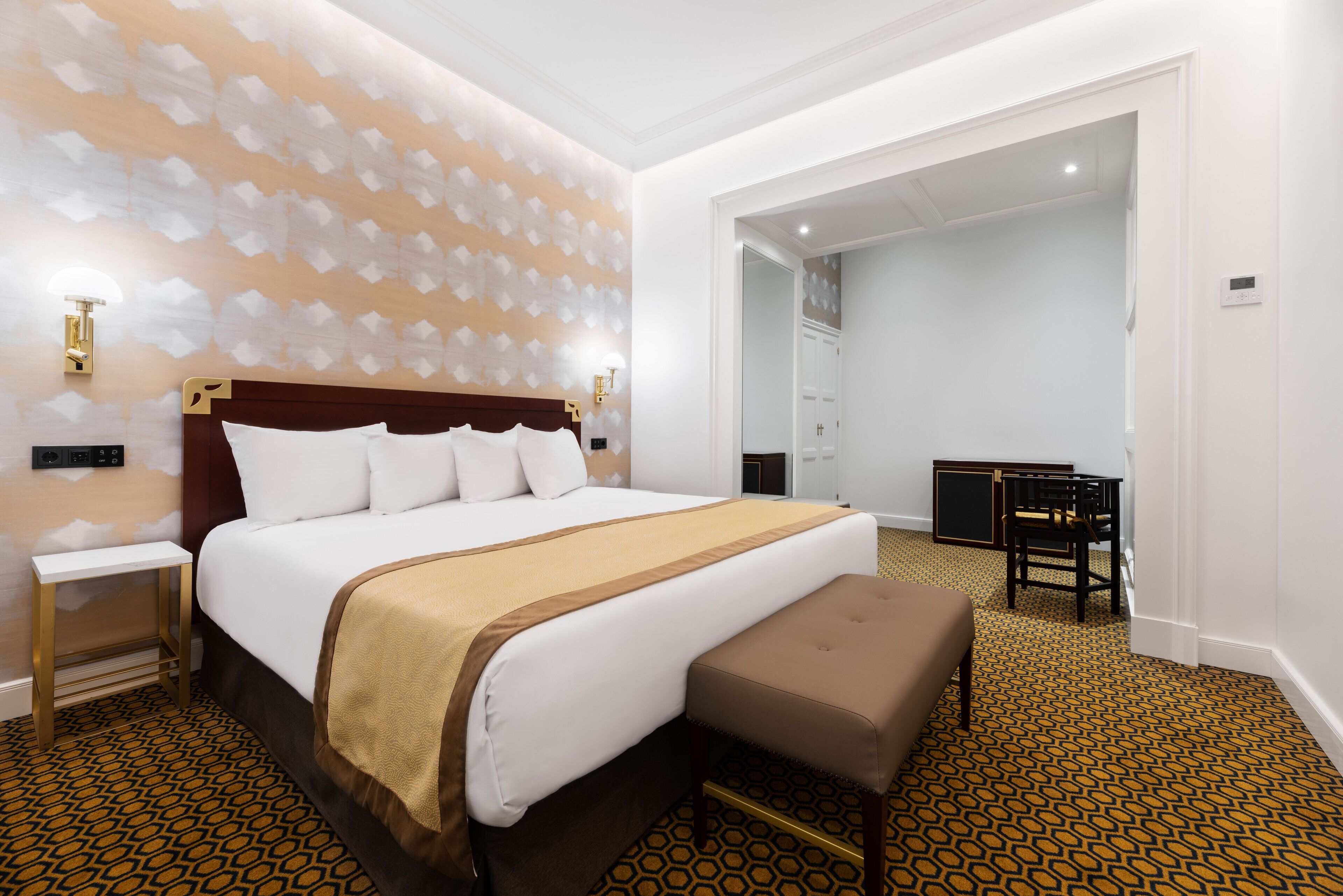 Una habitación de hotel con una cama grande, una mesita pequeña y un banco.