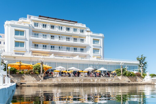A multi-story hotel with outdoor seating and a waterfront view.