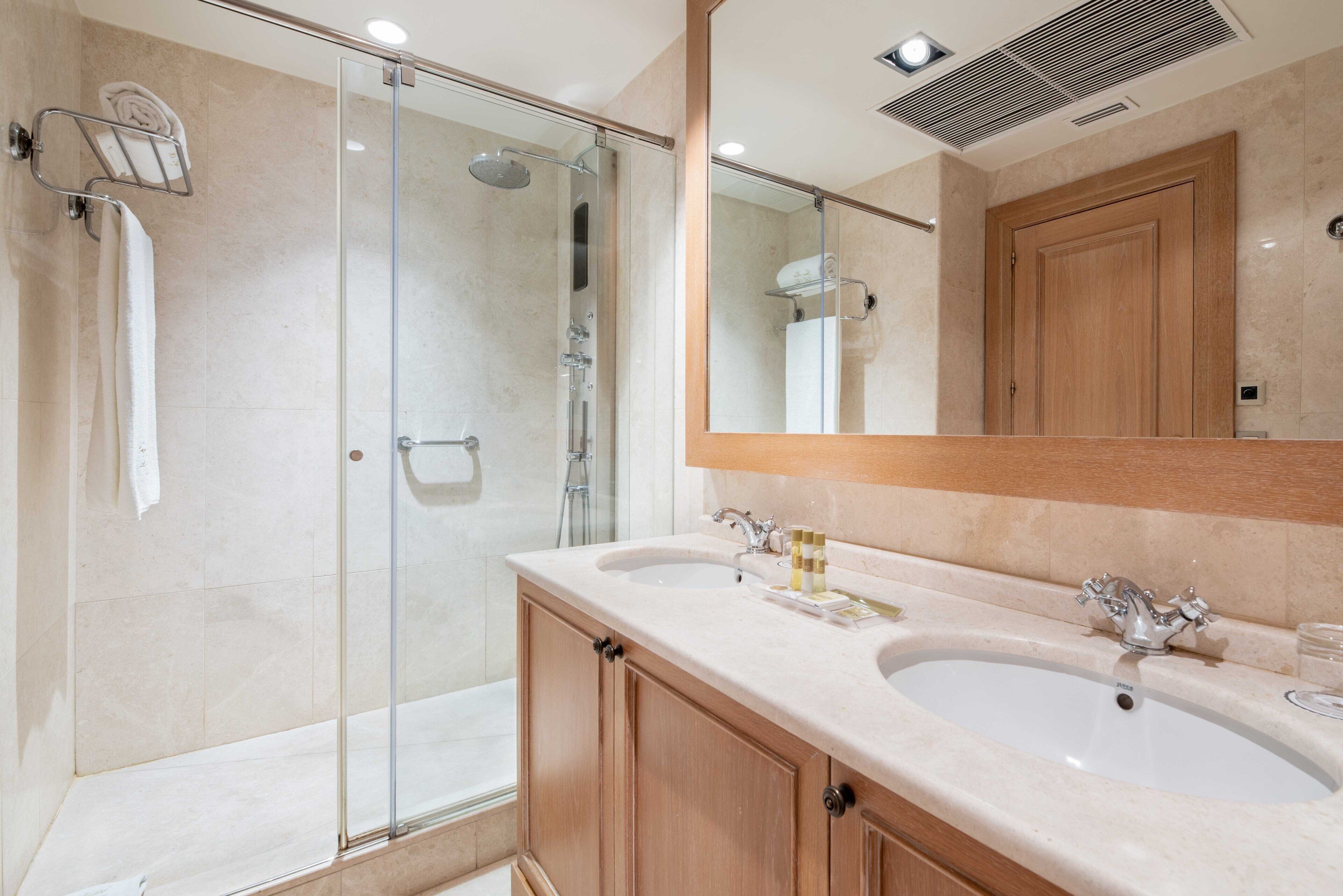 A modern bathroom with a glass-enclosed shower, two sinks, and a large mirror.