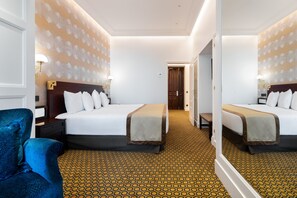 Une chambre d’hôtel avec un grand lit, une table de chevet, une chaise et un tapis à motifs géométriques.