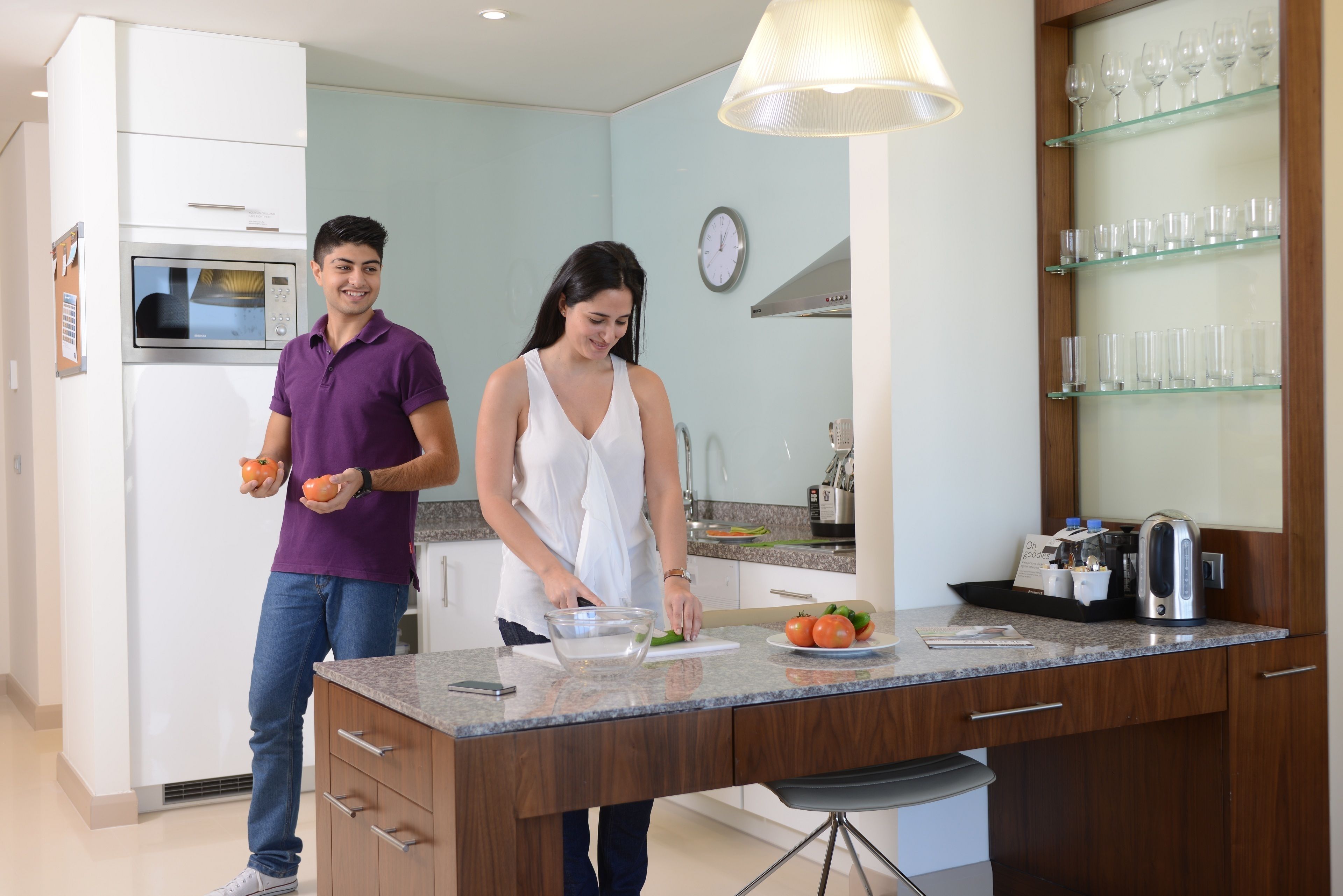 A modern kitchen with a built-in microwave, a coffee maker, and a glass display shelf.