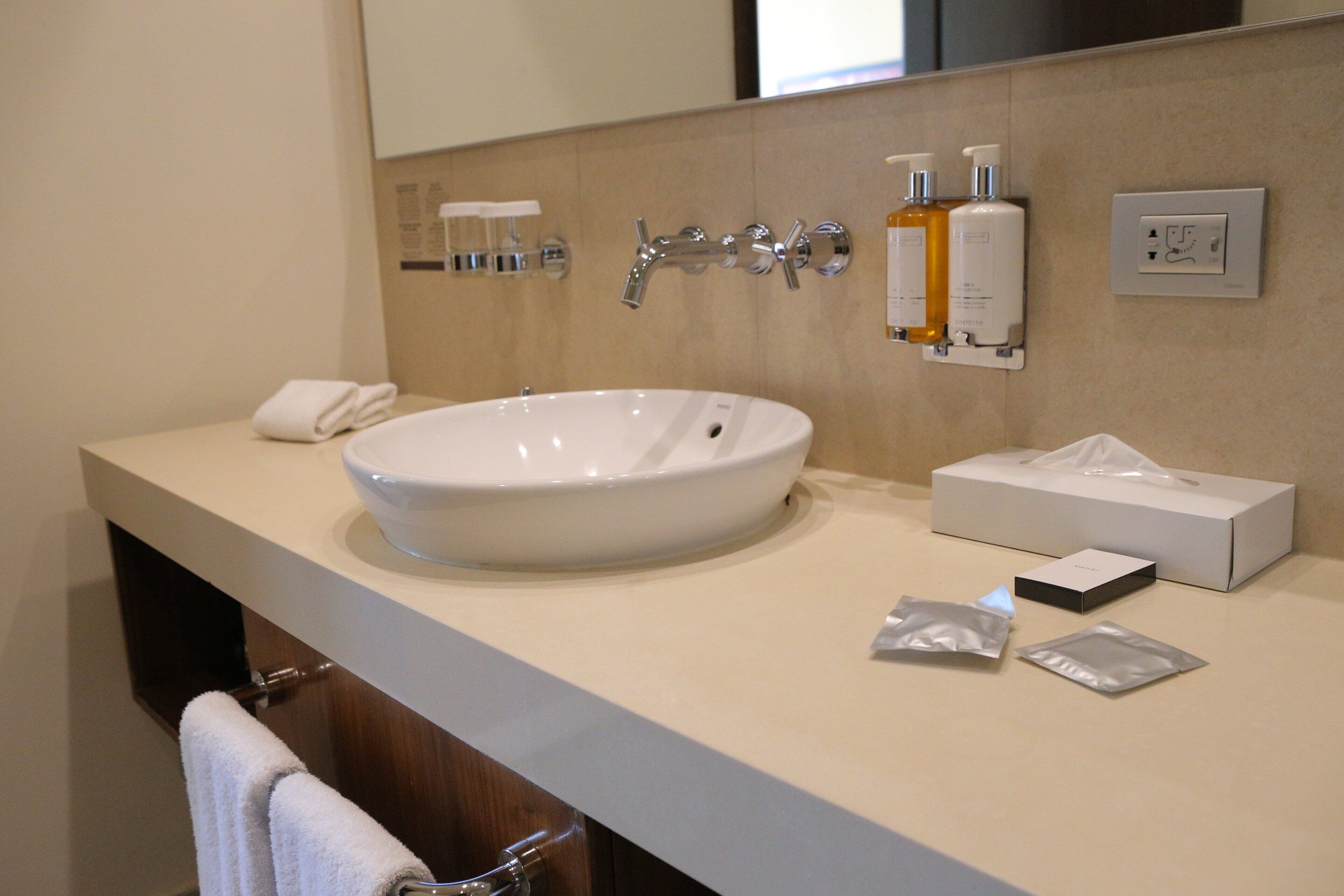 A bathroom with a large white sink, a towel rack, a mirror, and toiletries on the wall.