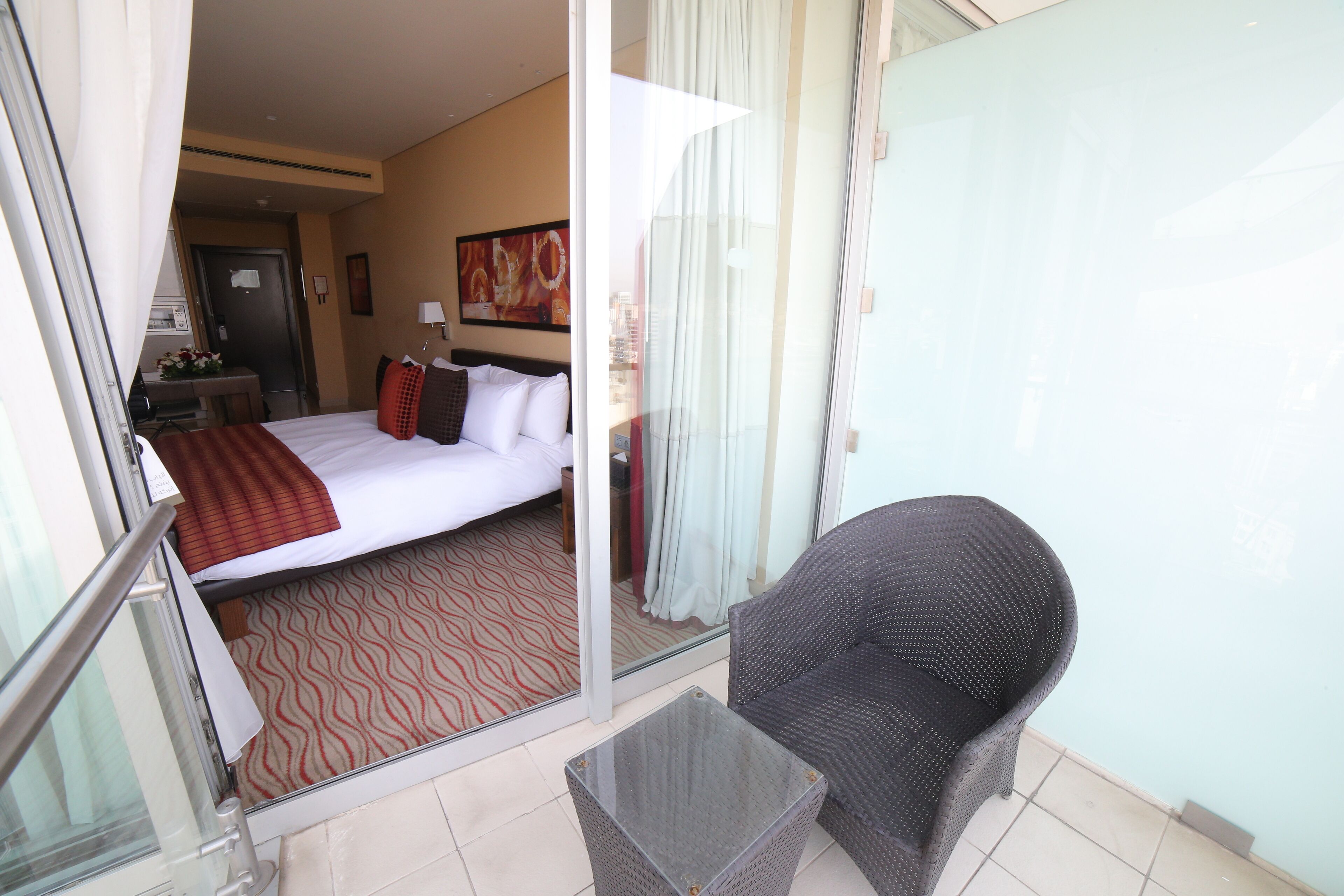 A hotel room with a bed, a small table, a chair, and a glass door leading to a balcony.