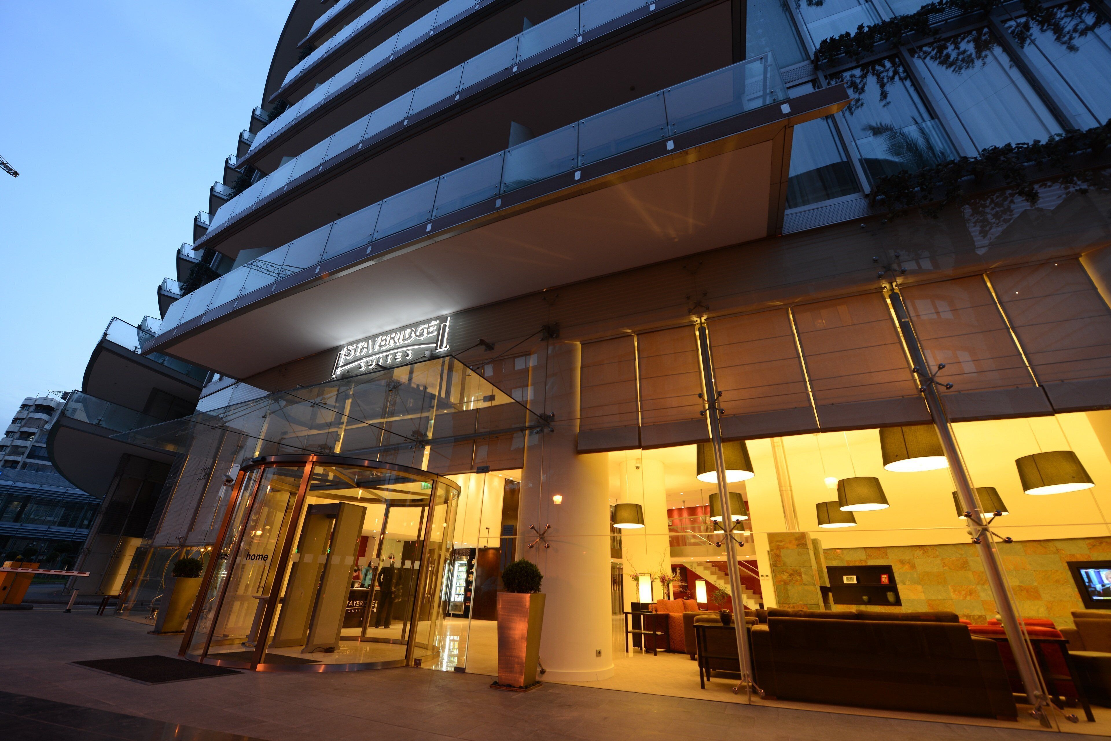 L’entrée d’un hôtel, avec une façade en verre, une enseigne indiquant « St. Bridge Suites », et un espace de réception doté de sièges.
