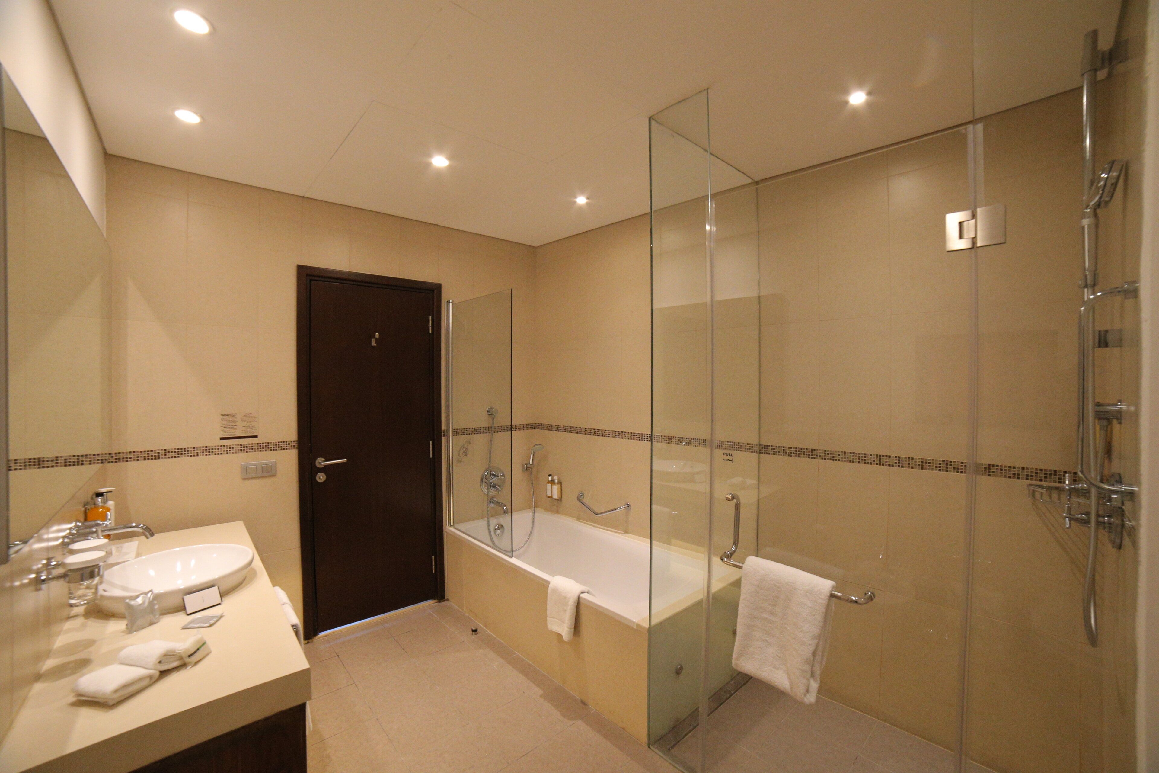 Un baño moderno con ducha envuelta en vidrio, una bañera independiente y un lavamanos con toallero.
