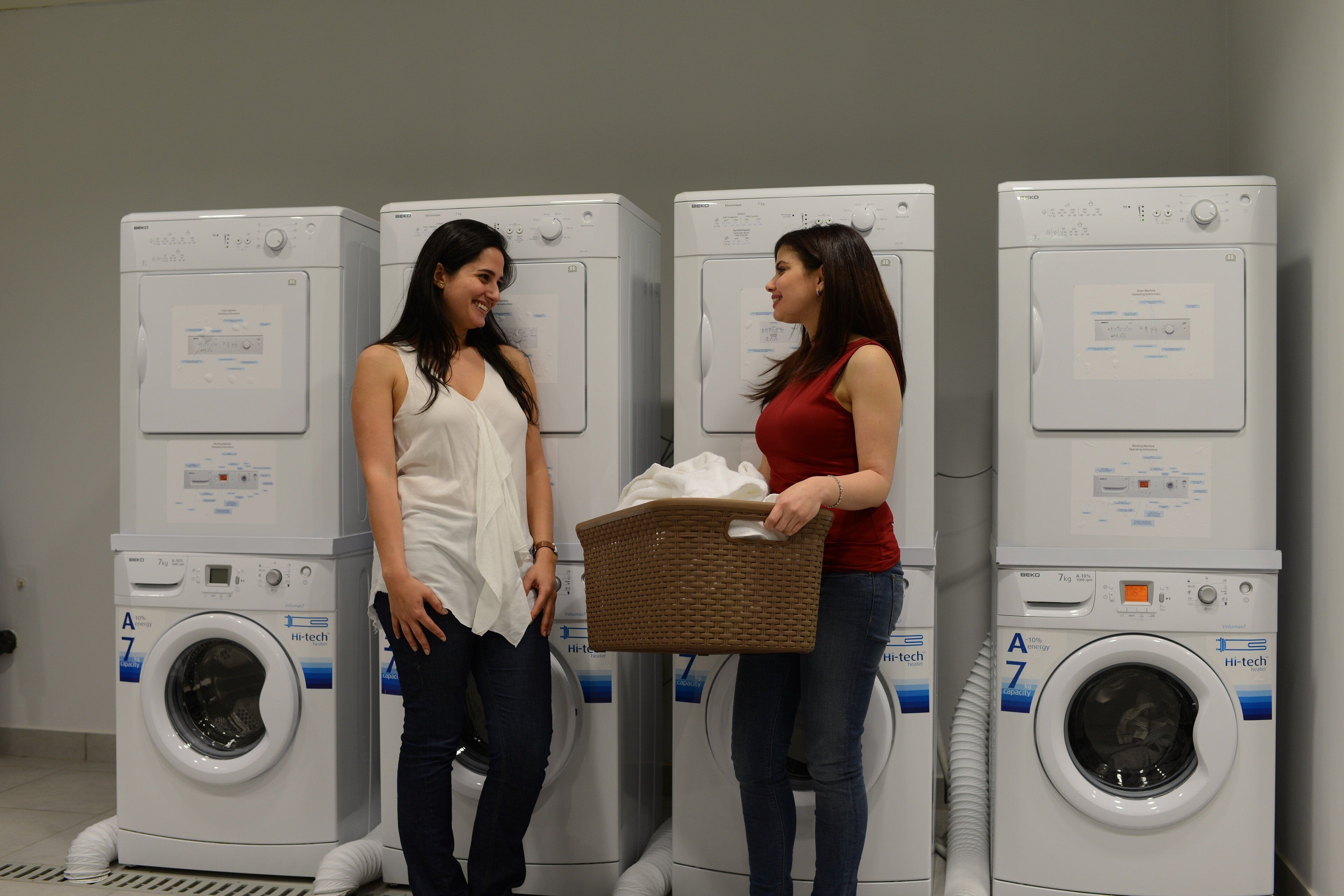 Two people standing in front of a row of white washing machines with capacity labels.