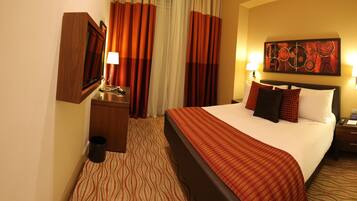 A hotel room with a bed, a nightstand with a lamp, a telephone, and a painting on the wall.