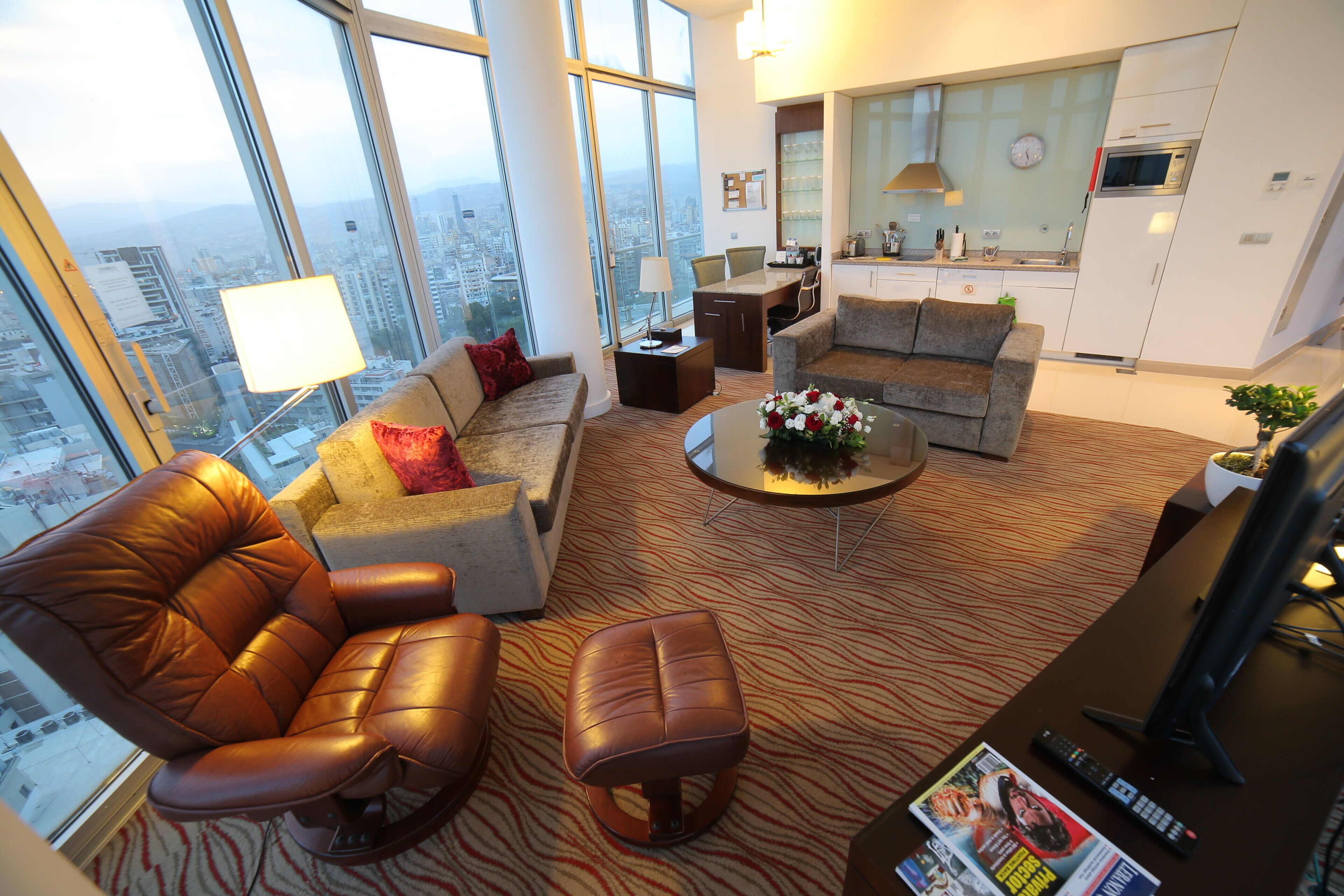 Een moderne woonkamer met een leren bank, een salontafel en een uitzicht op de stad door grote ramen.