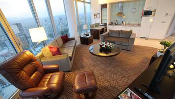 A modern living room with a leather sofa, a coffee table, and a view of the city through large windows.
