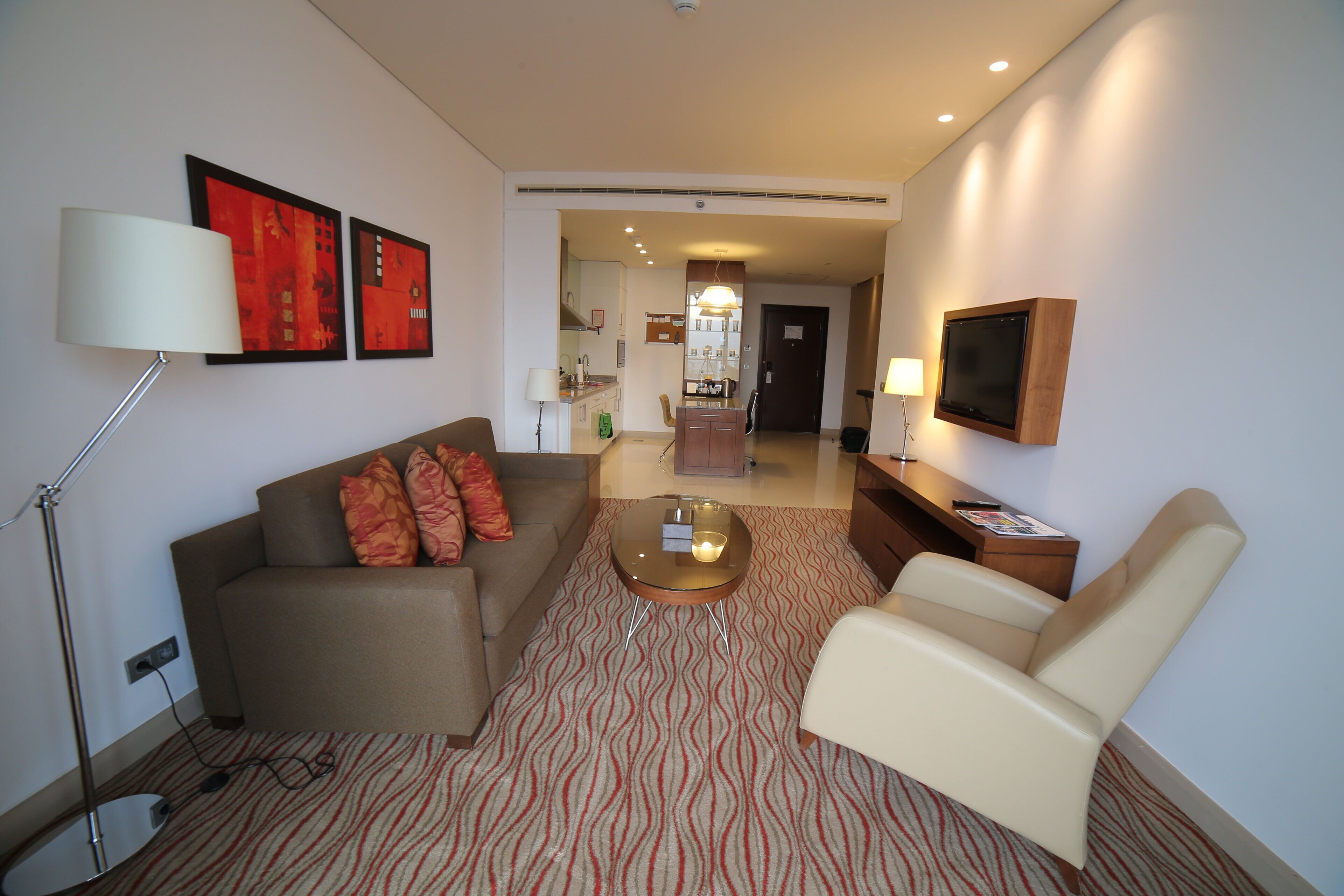 Ein modernes Wohnzimmer mit Sofa, Sessel, Couchtisch und einem an der Wand befestigten Flachbildfernseher.