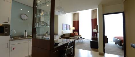 A modern hotel room with a kitchen area, a dining table, a sofa, and a bed.