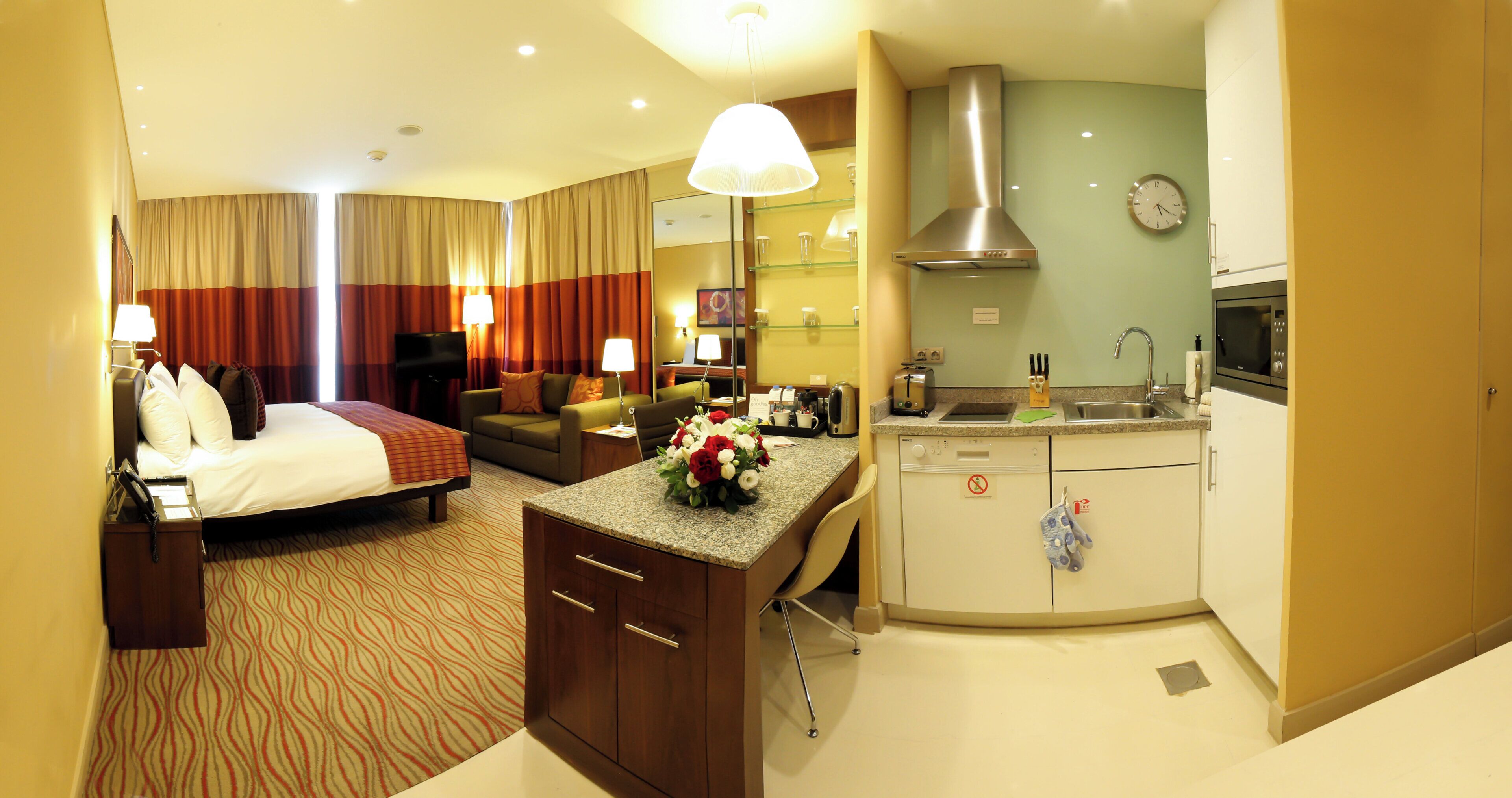 A hotel room with a bed, a desk, a kitchenette, and a living area.