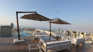 En tagterrasse med hvide møbler, et glasbord og parasoller.