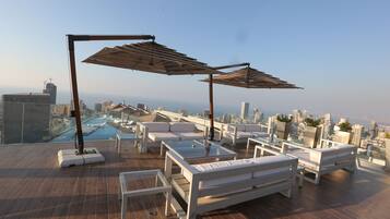 Relax on the rooftop with a panoramic city view, featuring a spacious seating area, umbrellas, and an infinity pool.