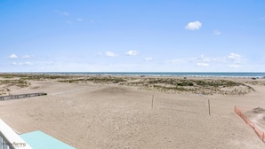 A beach view with a wooden walkway leading to the water, a sandy area with sparse vegetation, and a clear sky. - Beau Rivage Beach Resort (Wildwood Crest)