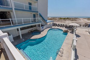 A pool area with a view of the beach, a staircase, and lounge chairs.