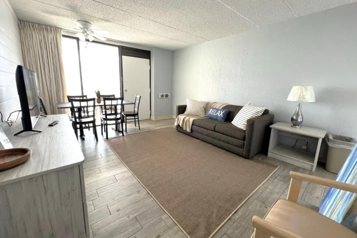 A modern living room with a sofa, a coffee table, a TV, and a dining area with chairs and a table.