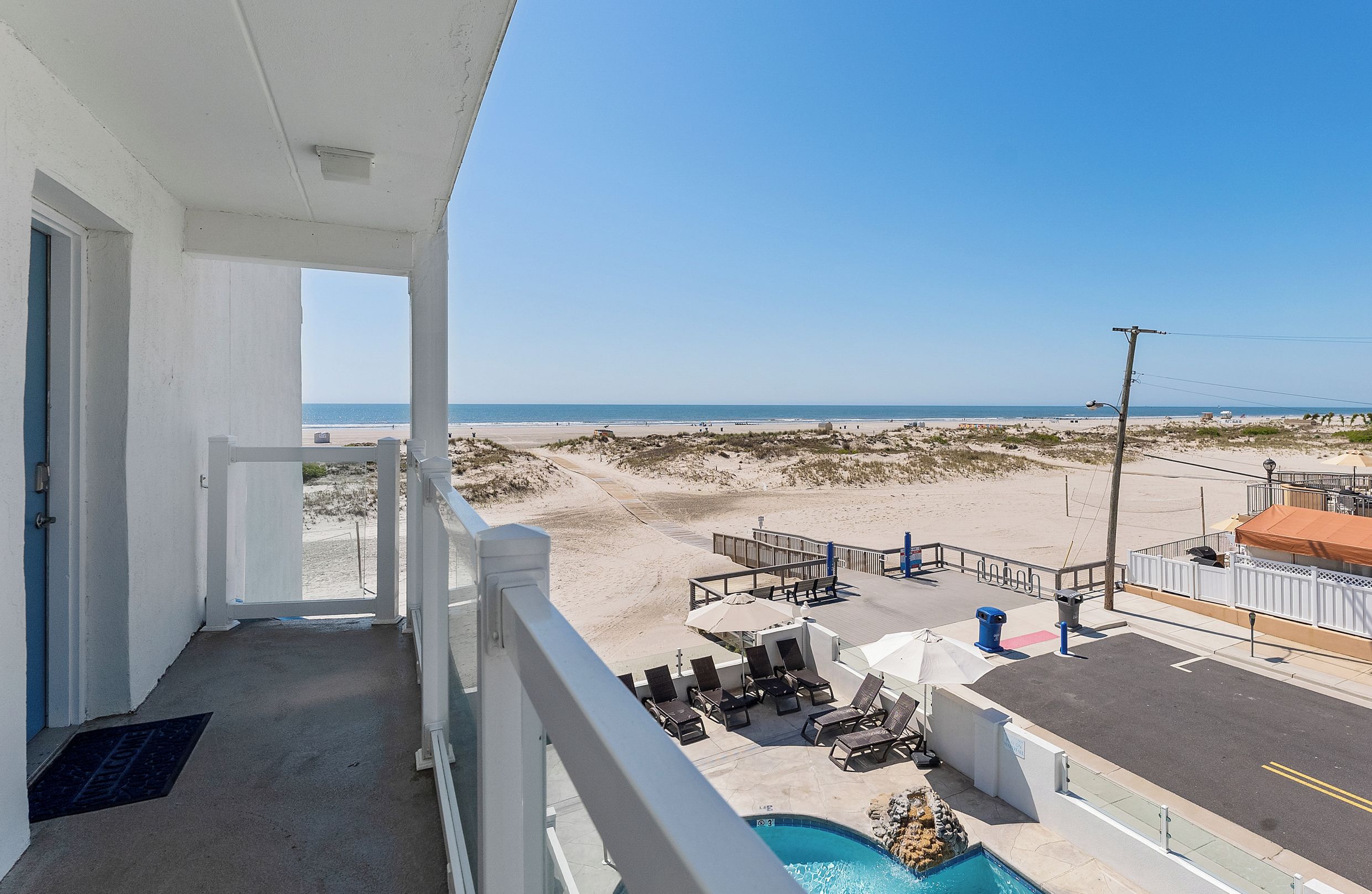 A balcony with a view of a beach and a pool area.