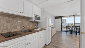 A modern kitchen with white cabinets, a granite countertop, a microwave, and a refrigerator. - Beau Rivage Beach Resort (Wildwood Crest)