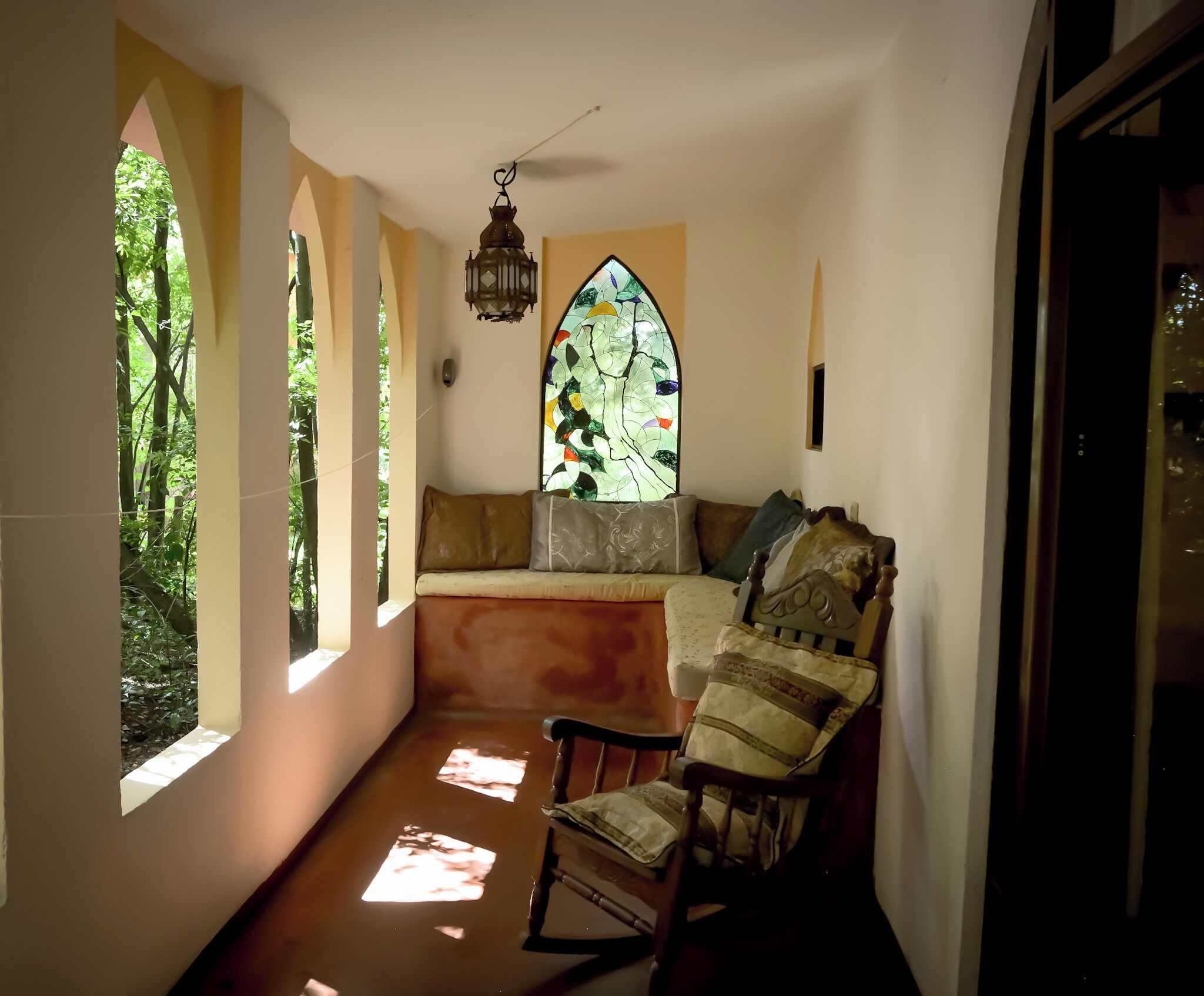 Una habitación acogedora con un banco, una silla de madera, un ventanal con vitrales y un farol colgante.