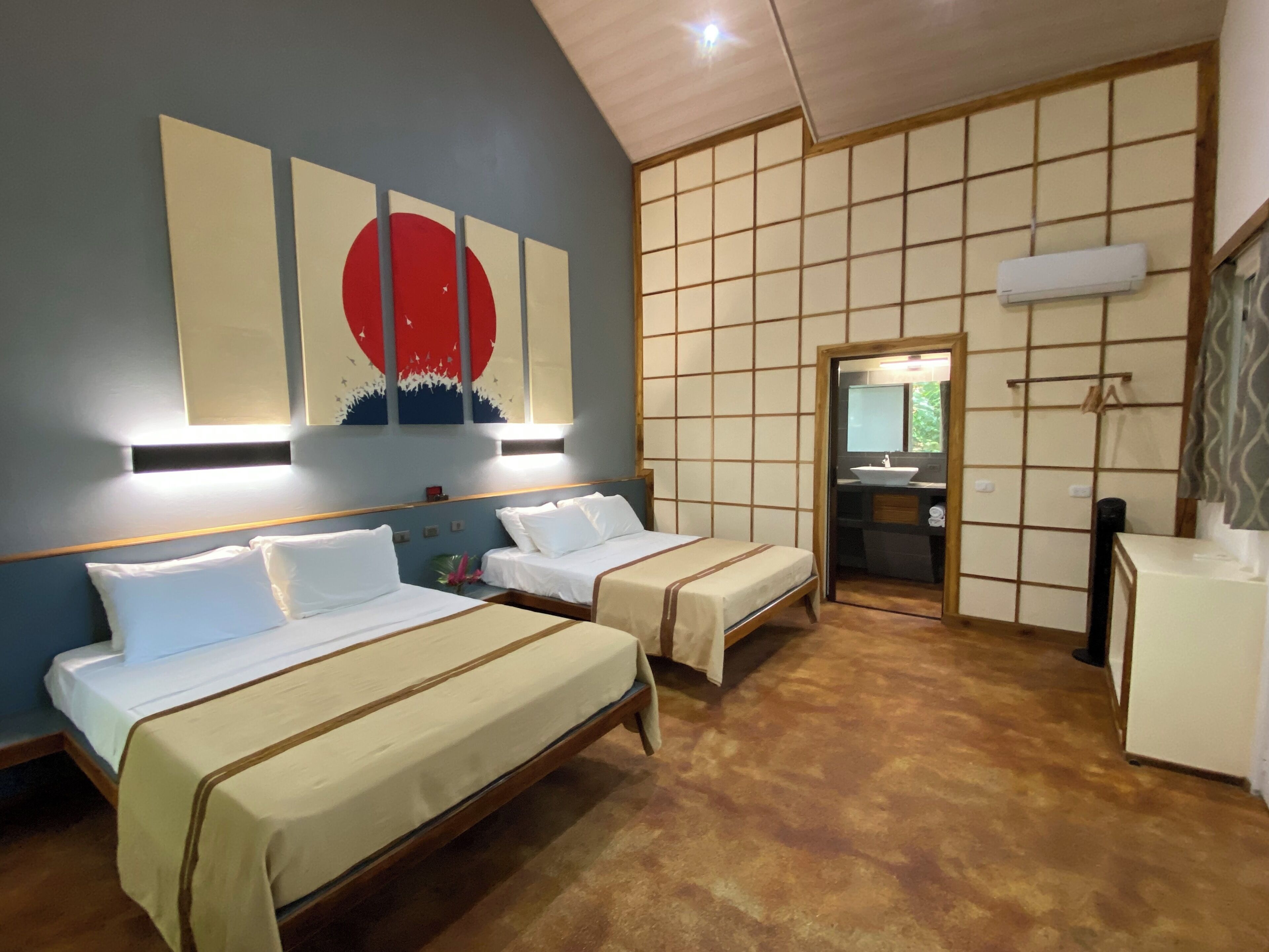 A hotel room with two beds, a large wall painting, a traditional Japanese sliding door, and a small bathroom.