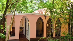 Un bâtiment rose, doté de fenêtres en arc de cercle et surmonté d’un dôme, entouré d’arbres.
