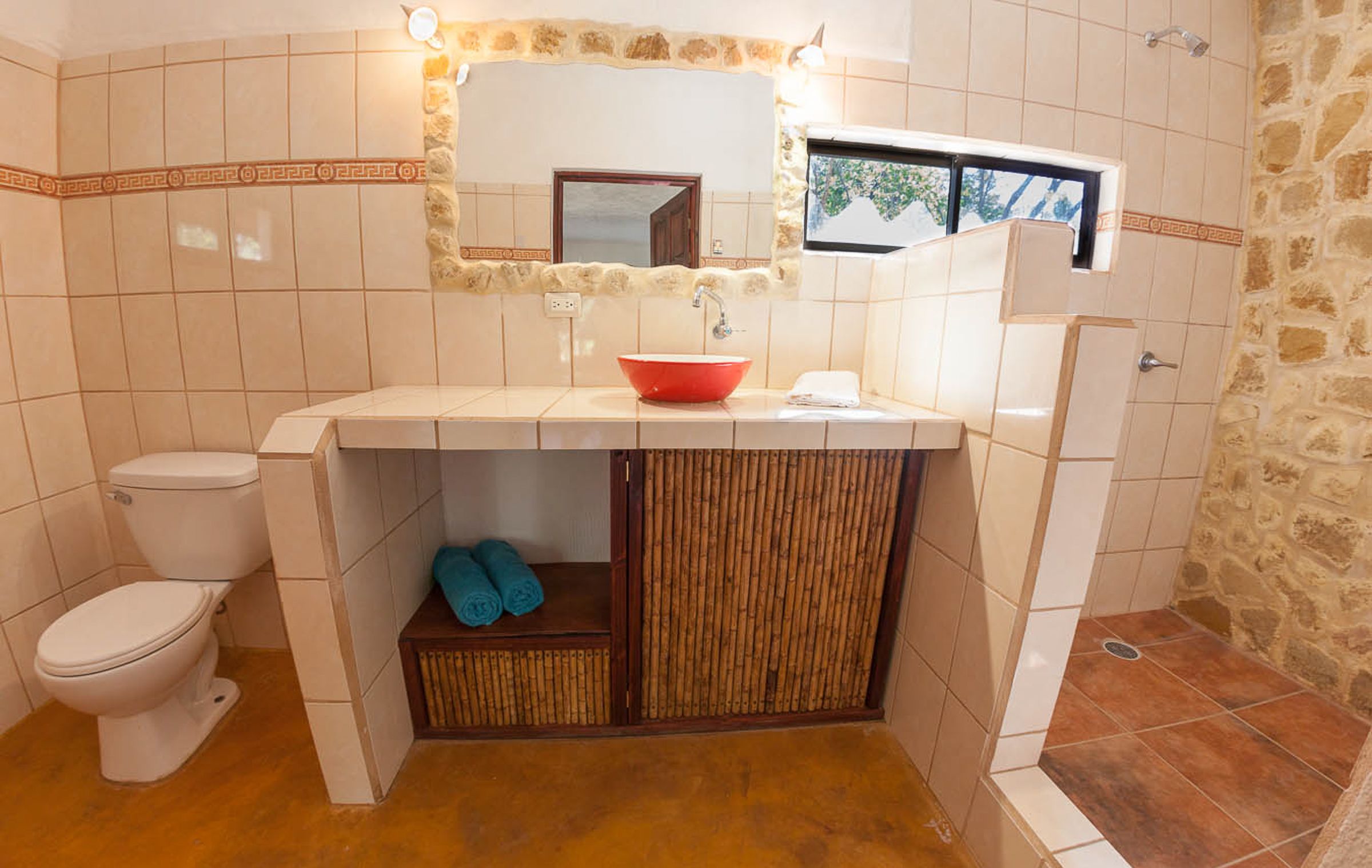 Ein Badezimmer mit Toilette, Waschbecken in Rot, einem Spiegel und einer Duschkabine.