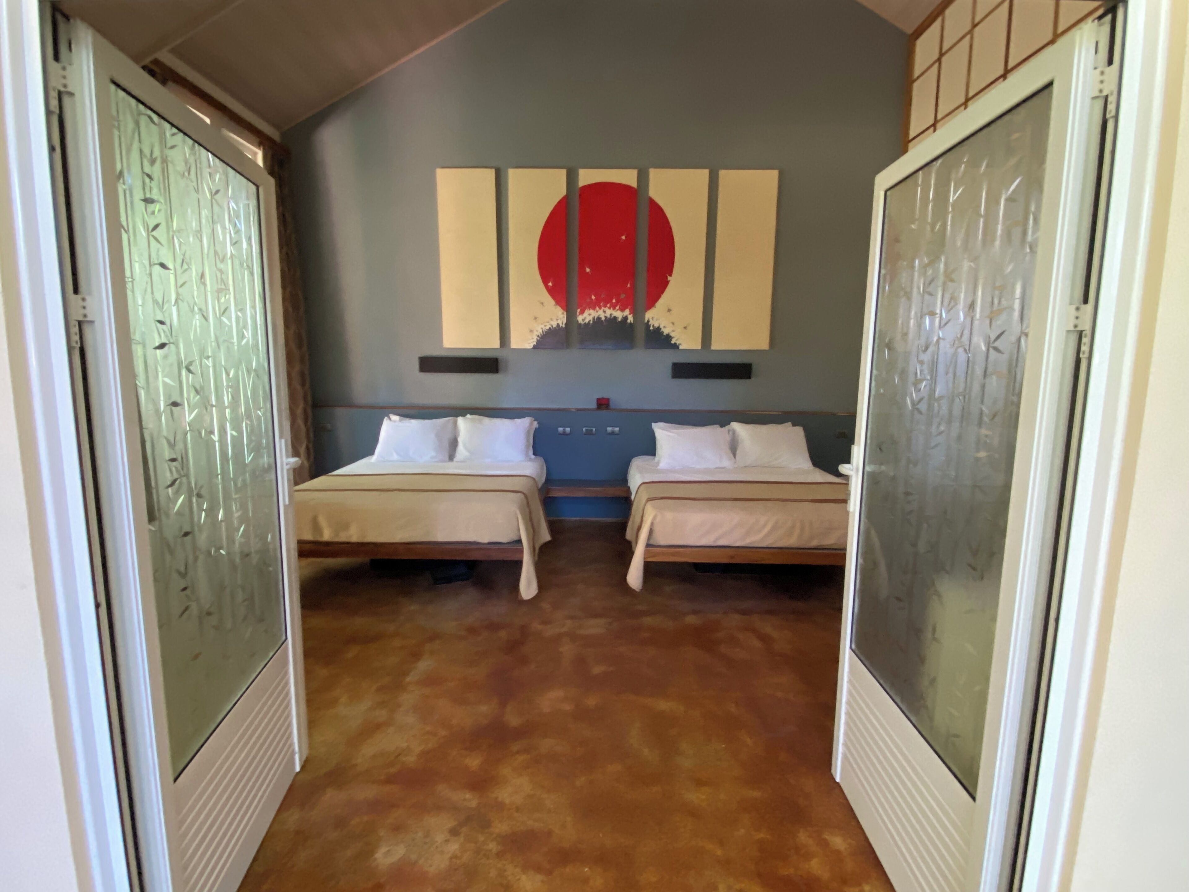 Une chambre avec deux lits, un grand tableau abstrait au mur et un rideau à motifs.