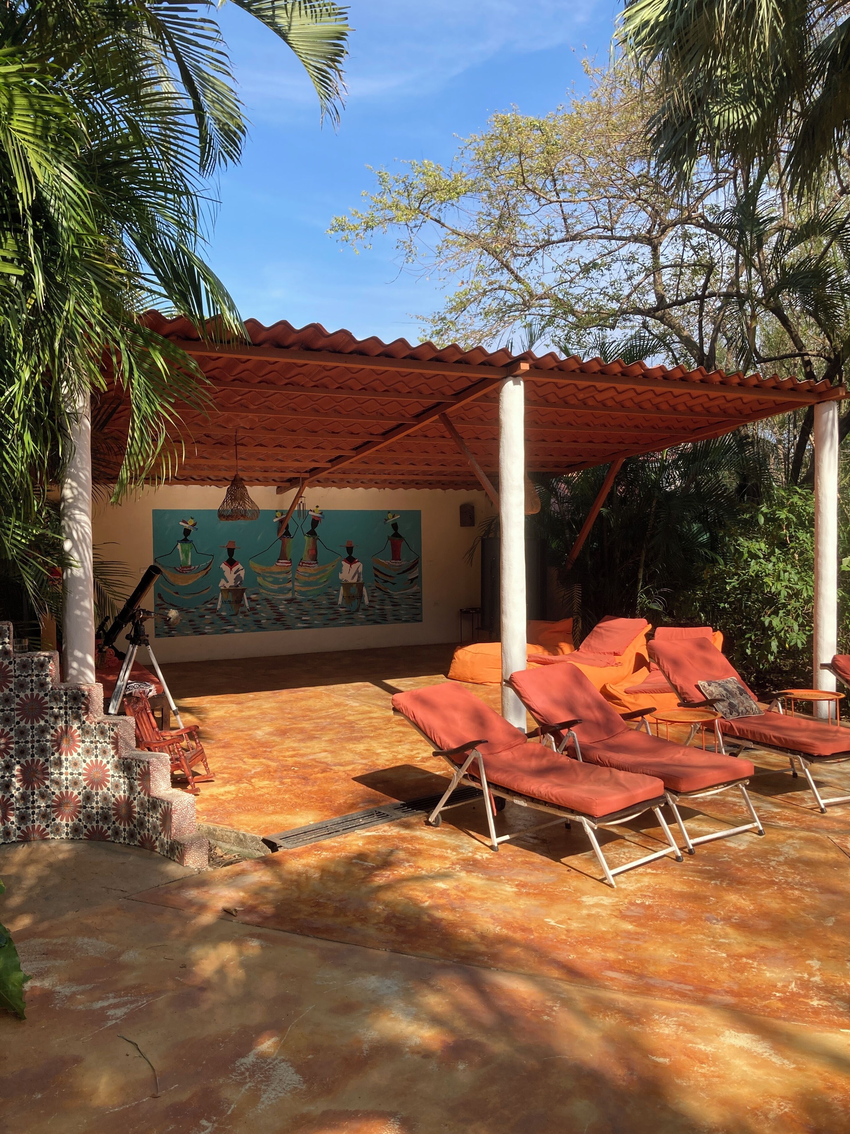 A covered outdoor seating area with red lounge chairs and a mural on the wall.