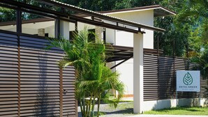 Un edificio moderno con listones horizontales, una palmera y un cartel que anuncia Hotel Green Playa Jacón.