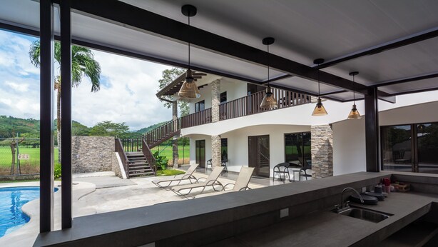 Una casa moderna con piscina, mobiliario exterior y un balcón.