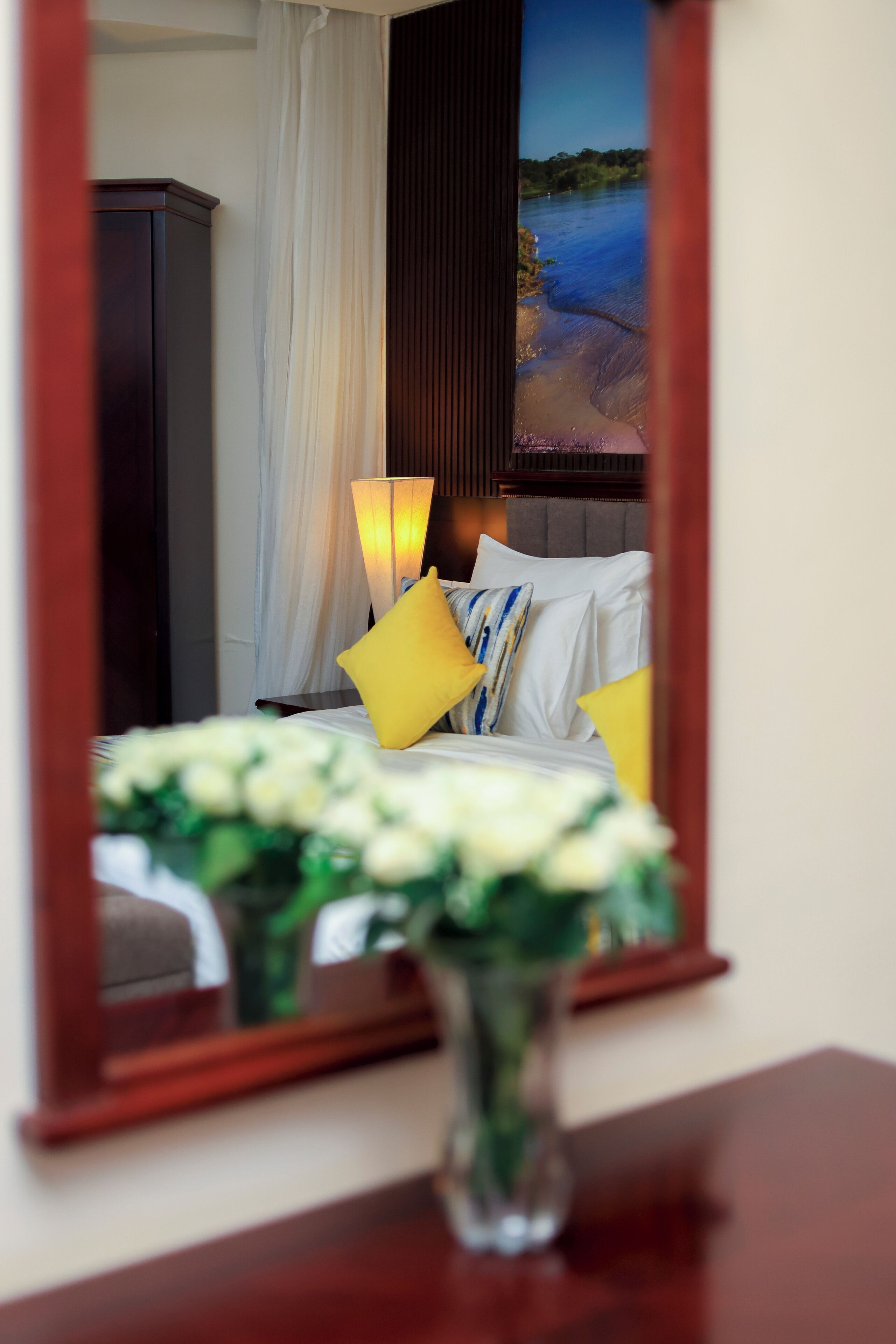 Una habitación de hotel con cama, mesita de noche, lámpara y un jarrón con flores.