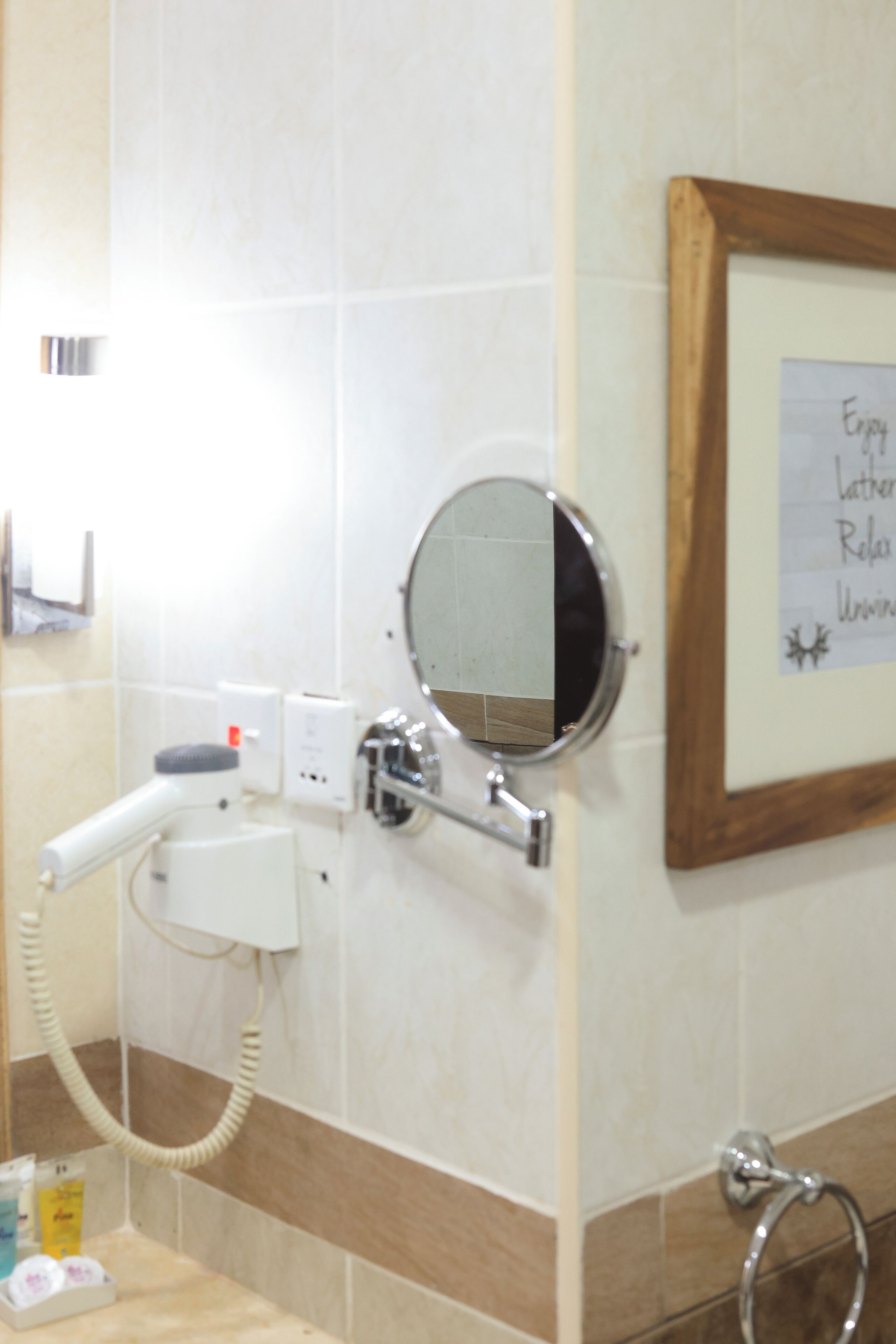 A bathroom with a hairdryer, a mirror, and a framed sign on the wall.