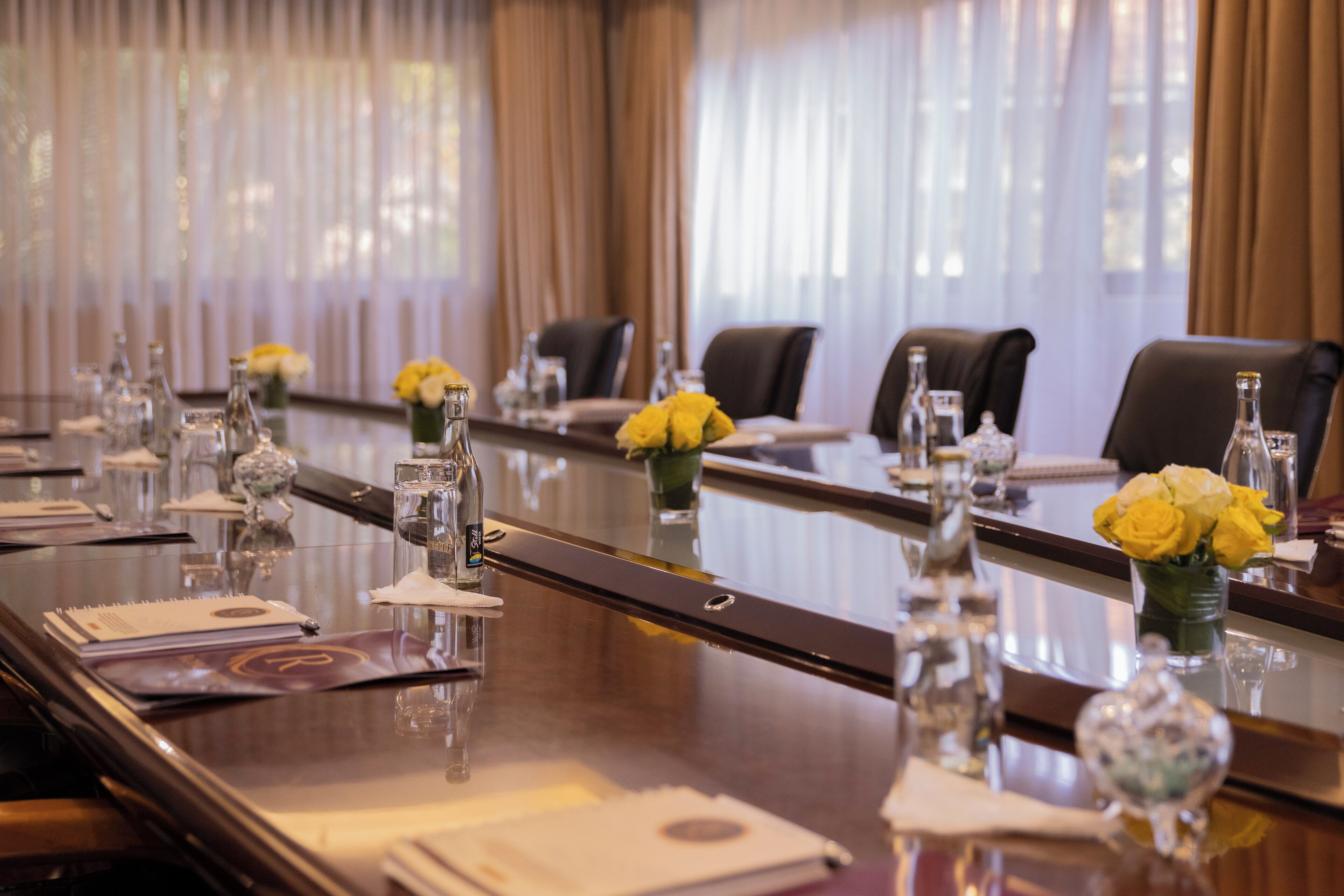 Une table de conférence entourée de chaises, agrémentée de vases remplis de fleurs jaunes et de divers objets en verre.