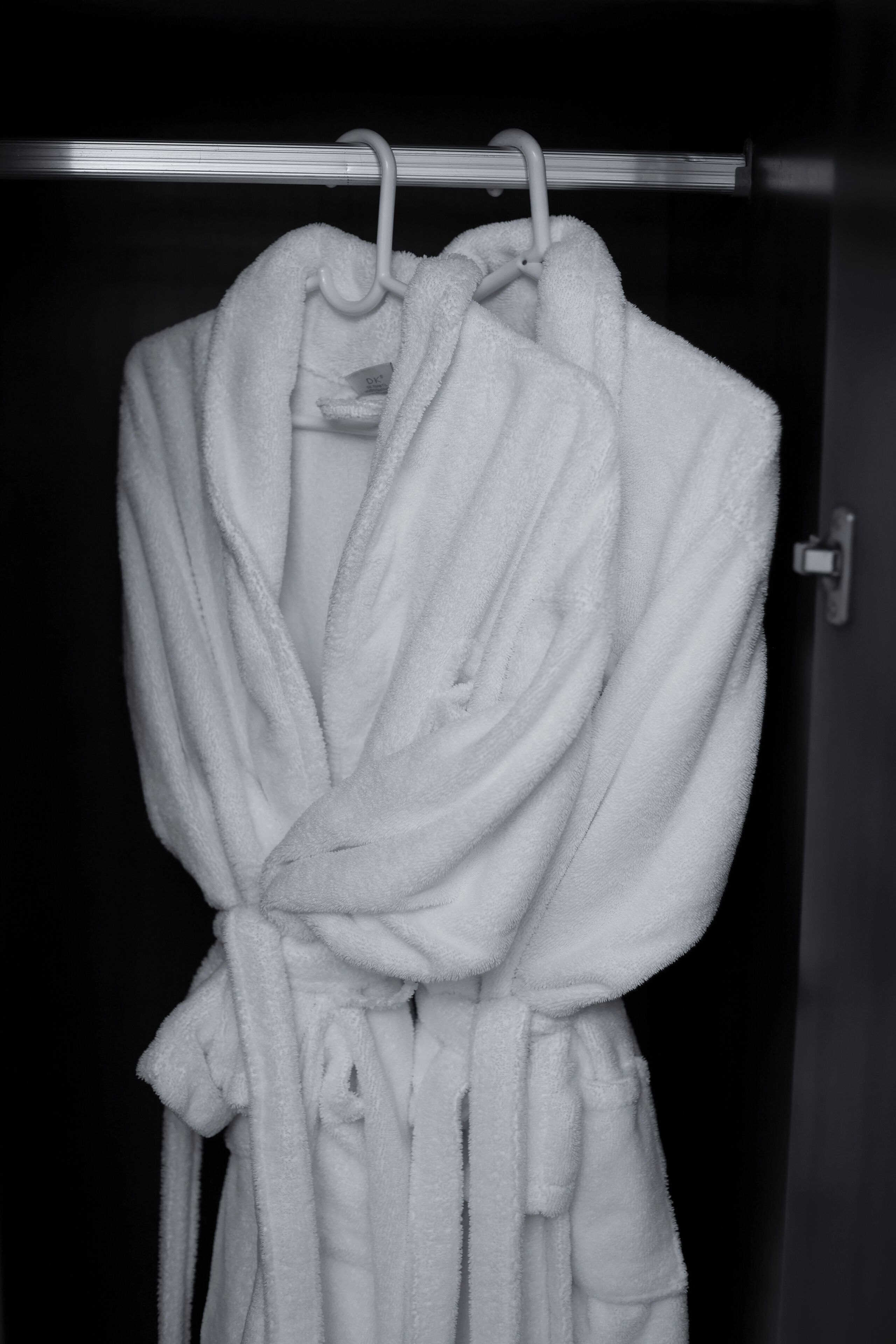 A white bathrobe hanging on a metal rack in a dark room.