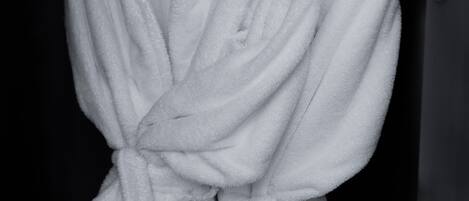 A white bathrobe hanging on a metal rack in a dark room.