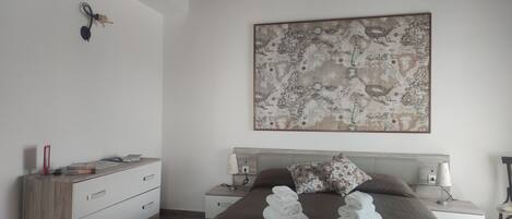 A bedroom with a bed, a wooden dresser, a nightstand, and a wall map.