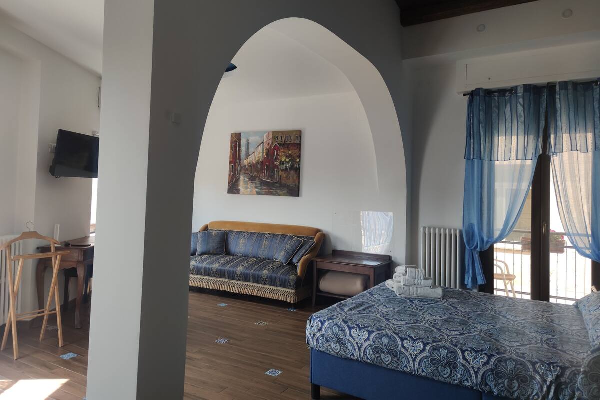 A bedroom with a bed, a sofa, a TV, and a painting on the wall.