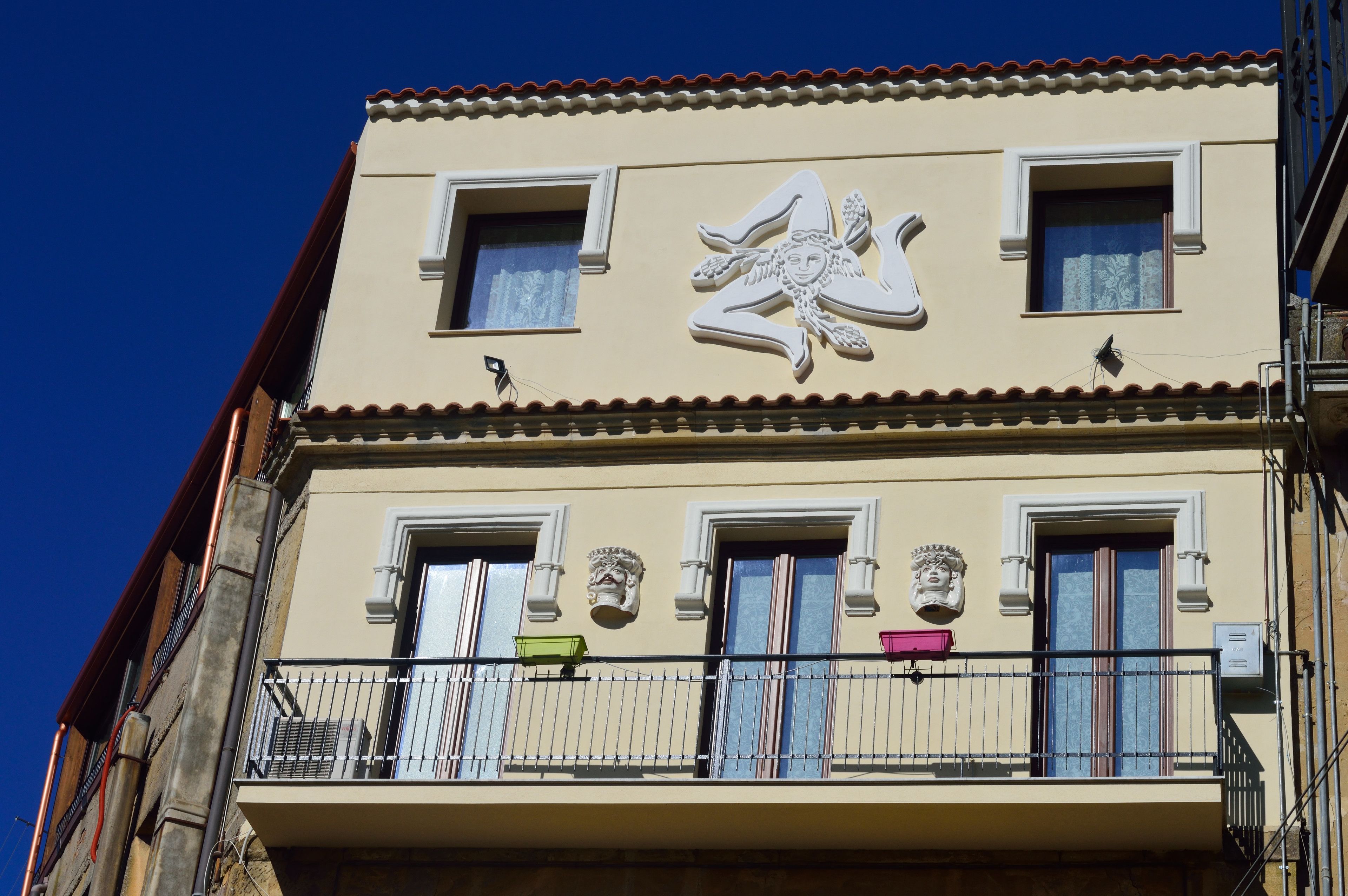 Un edificio con balcón, un emblema decorativo y un ventanal con cortina.