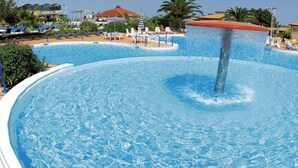 Une grande piscine circulaire avec une fontaine au centre, entourée de chaises longues et de parasols.