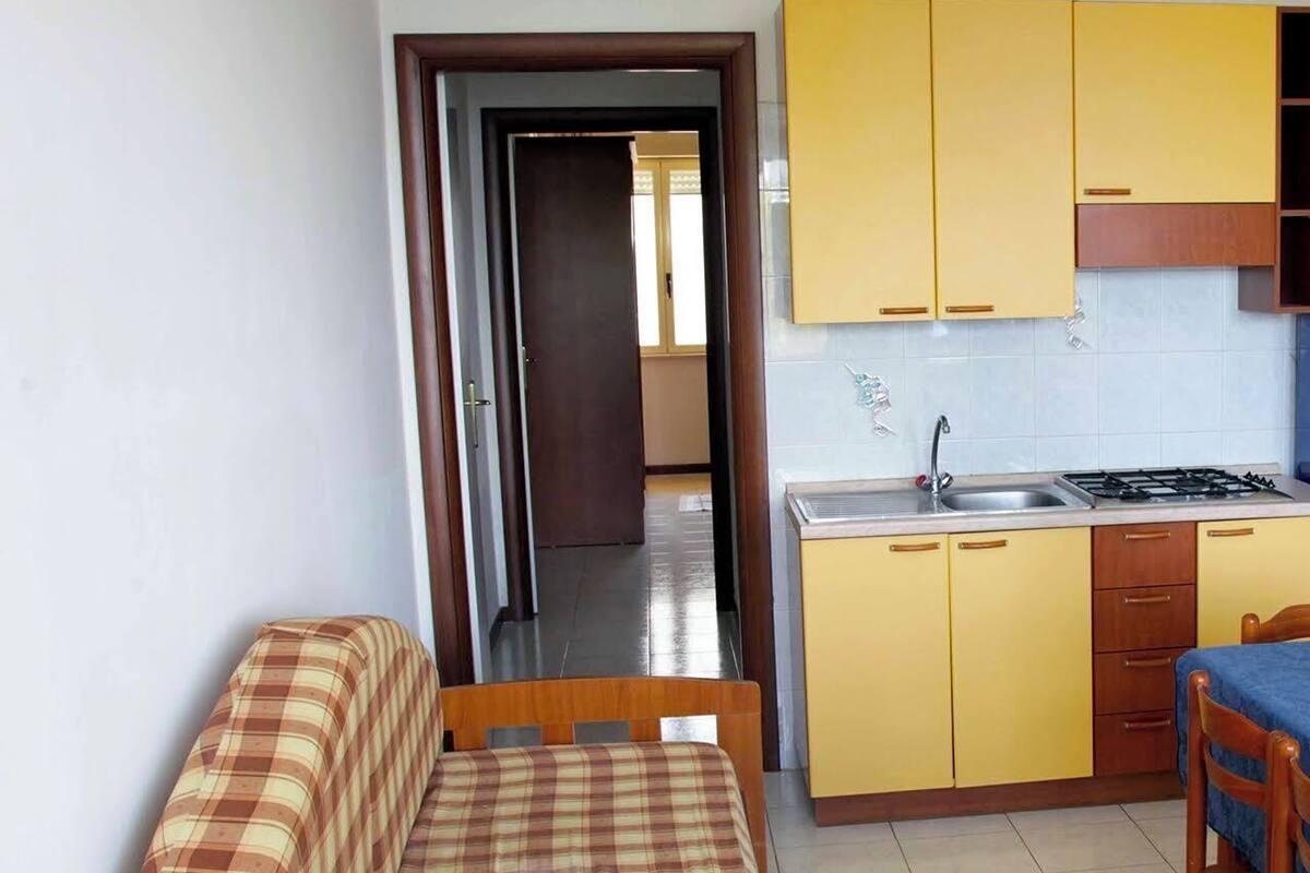 A compact kitchen with yellow cabinets, a sink, and a stove. There is a wooden bench with a plaid cover in the foreground.