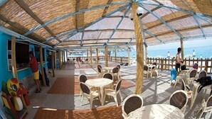 Un café en plein air avec des parasols en chaume, des chaises et des tables en plastique.