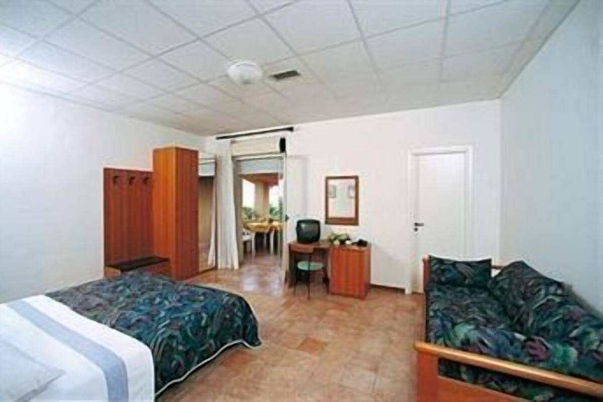 A room with two beds, a desk, a chair, a television, and a door.