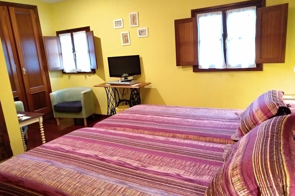 Une chambre avec deux lits, un bureau, une chaise, une télévision et une fenêtre avec des rideaux.